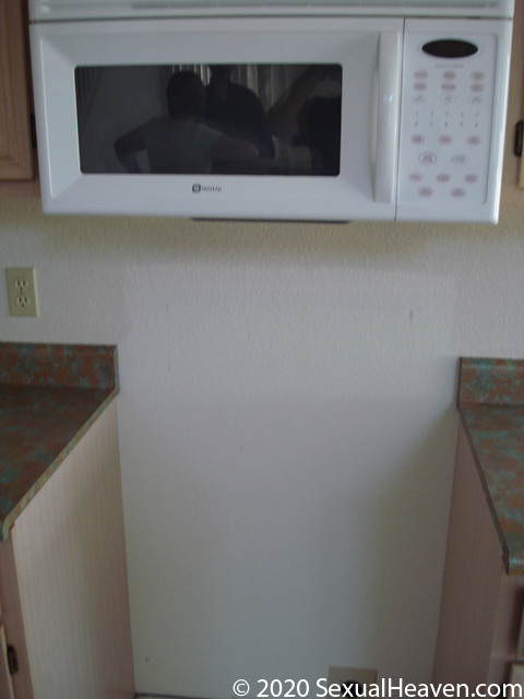 A white microwave hanging above an area for a stove.